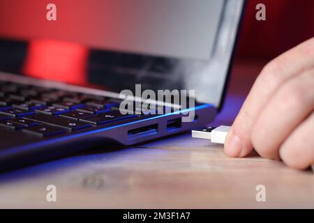 insertion du câble usb dans l'ordinateur portable sur une table et sur un arrière-plan coloré Banque D'Images