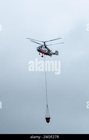 Un hélicoptère d'incendie transporte un conteneur d'eau pour éteindre un incendie dans un bâtiment de production Banque D'Images