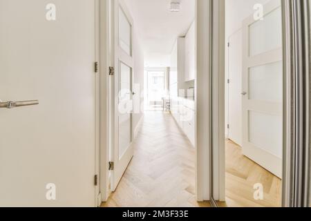 un long couloir avec des murs blancs et du parquet de chaque côté, menant à une porte ouverte Banque D'Images