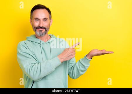 Photo du promoteur homme d'âge moyen brunet cheveux tenir le doigt de paume point mockup meilleure option bon marché marque de produit isolé sur fond jaune de couleur Banque D'Images