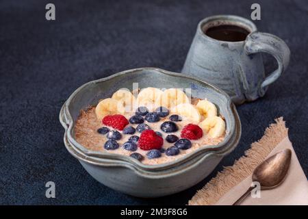 Flocons d'avoine coupés en acier biologique à base de plantes, recouverts de fruits dans un beau bol bleu avec du café dans une tasse assortie; espace de copie Banque D'Images