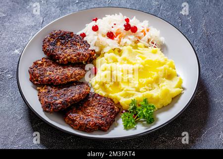 pâtés de foie frits hachés, juuhamaksapihvit finlandais, avec purée de pommes de terre, choucroute et canneberges sur une assiette sur une table en béton Banque D'Images