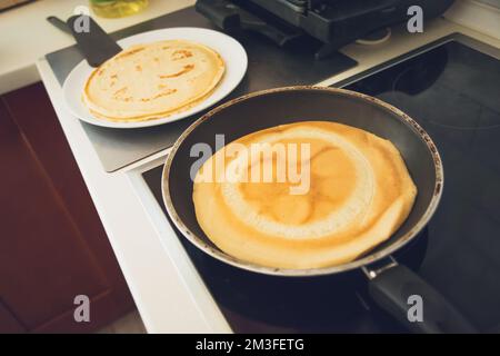 Faire frire des crêpes dans une poêle sur une table de cuisson à induction noire Banque D'Images