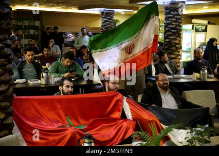 Téhéran, Téhéran, Iran. 14th décembre 2022. Les hommes iraniens détiennent un drapeau palestinien (R), un drapeau marocain (L) et un drapeau iranien (TOP) tandis qu'un groupe de fans palestiniens assis derrière eux pendant la demi-finale du match Qatar 2022 de la coupe du monde de la FIFA entre la France et le Maroc, au café Nakhlestan dans le centre-ville de Téhéran, 14 décembre 2022. Les fans d'Iran, du Liban, du Yémen, de Syrie et de Palestine se rassemblent au café de Nakhlestan, qui est géré et détenu par l'organisation artistique et médiatique Owj (IRGS) du corps des Gardiens de la révolution islamique, pour soutenir l'équipe nationale marocaine. Après la victoire contre le Portugal au Qatar o Banque D'Images