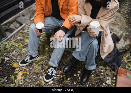 Vue rognée d'un jeune couple élégant tenant des tasses en papier sur la terrasse du café, image de stock Banque D'Images