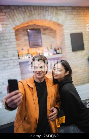Couple multiethnique souriant prenant selfie sur téléphone portable dans le café, image de stock Banque D'Images