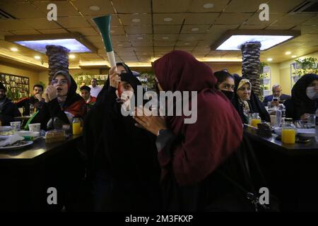 Téhéran, Téhéran, Iran. 15th décembre 2022. Les fans iraniens féminins voilés réagissent alors que l'un d'eux tient une corne tout en regardant la demi-finale du match de la coupe du monde de la FIFA, Qatar 2022 entre la France et le Maroc à l'écran, au café Nakhlestan dans le centre-ville de Téhéran, en Iran, 15 décembre 2022. Les fans d'Iran, du Liban, du Yémen, de Syrie et de Palestine se rassemblent au café de Nakhlestan, qui est géré et détenu par l'organisation artistique et médiatique Owj (IRGS) du corps des Gardiens de la révolution islamique, pour soutenir l'équipe nationale marocaine. Après la victoire contre le Portugal au Qatar sur 10 décembre, les Marocains ont porté des drapeaux palestiniens à Banque D'Images