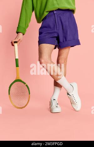 Image courte des jambes de l'homme dans un short et des baskets, penchée sur une raquette de tennis isolée sur fond rose. Vintage Banque D'Images