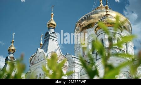 Vue de dessous d'une église blanche avec des dômes dorés. Attache. Vue à travers les feuilles vertes d'un arbre sur l'église orthodoxe et le ciel bleu Banque D'Images