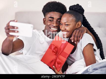 Nous avons besoin d'une photo de nous à l'occasion de notre premier anniversaire. une jeune femme tenant une boîte cadeau tout en prenant un selfie avec son petit ami. Banque D'Images
