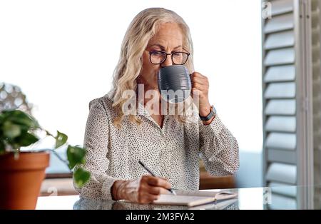 Un café fort vous permettra de continuer. une femme d'affaires très attirante qui boit du café tout en travaillant à la maison. Banque D'Images