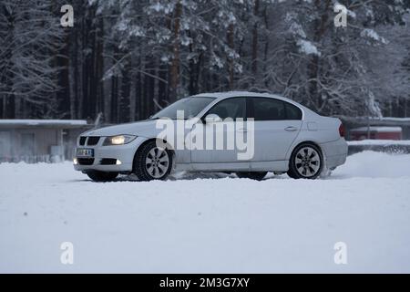 12-12-2022 Riga, Lettonie une voiture blanche garée dans la neige près d'une forêt d'arbres et d'un bâtiment avec une porte et des fenêtres rouges. . Banque D'Images