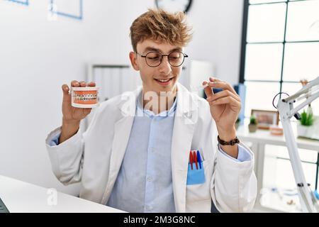Jeune homme caucasien portant un uniforme de dentiste tenant des supports et un outil d'alignement à la clinique Banque D'Images