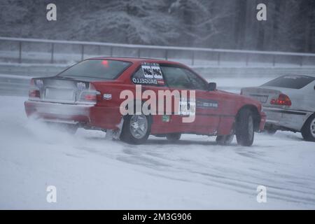 12-12-2022 Riga, Lettonie une voiture rouge roule dans la neige avec un panneau sur son capot et une voiture derrière elle. . Banque D'Images