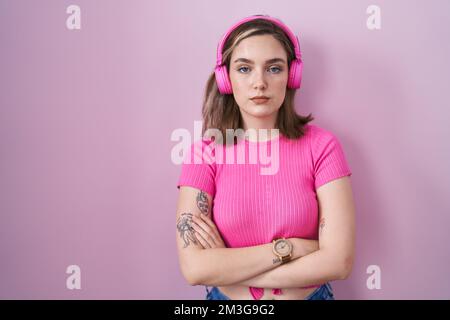 Femme blanche blonde écoutant de la musique en utilisant des écouteurs avec une expression sérieuse sur le visage. simple et naturel à regarder l'appareil photo. Banque D'Images