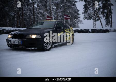 12-12-2022 Riga, Lettonie une voiture est garée dans la neige près des arbres et des drapeaux sur un poteau avec un drapeau sur lui. . Banque D'Images