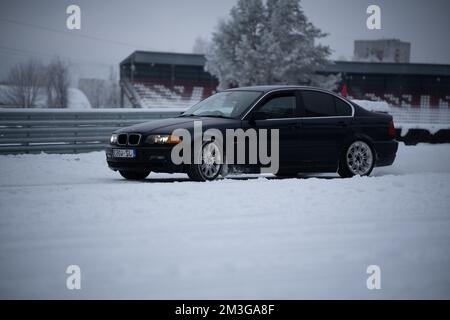 12-12-2022 Riga, Lettonie une voiture noire garée dans la neige près d'une clôture et d'un bâtiment avec un toit rouge et un toit rouge. . Banque D'Images