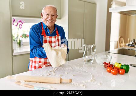 Homme âgé souriant confiant tenant la pâte avec les mains dans la cuisine Banque D'Images