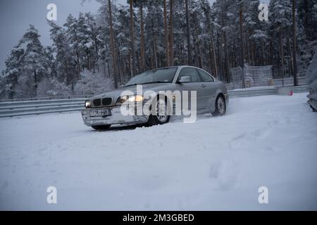 12-12-2022 Riga, Lettonie une voiture est garée dans la neige près d'une forêt d'arbres et d'une clôture avec un banc en arrière-plan. . Banque D'Images