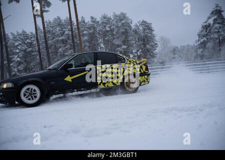 12-12-2022 Riga, Lettonie une voiture avec un dessin jaune et noir sur elle conduisant dans la neige en face d'une forêt avec des arbres. . Banque D'Images