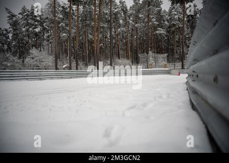 12-12-2022 Riga, Lettonie un champ enneigé avec une clôture et des arbres en arrière-plan et une borne incendie rouge en premier plan. . Banque D'Images