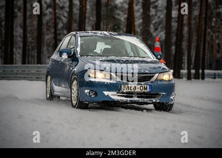 12-12-2022 Riga, Lettonie une voiture bleue traversant une forêt enneigée avec des arbres en arrière-plan et un feu rouge. . Banque D'Images