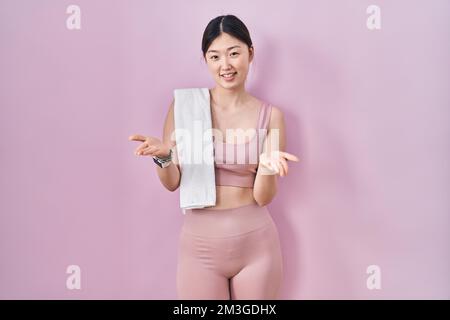 Jeune femme chinoise portant des vêtements de sport et une serviette souriante offrant des mains souriantes donnant assistance et acceptation. Banque D'Images