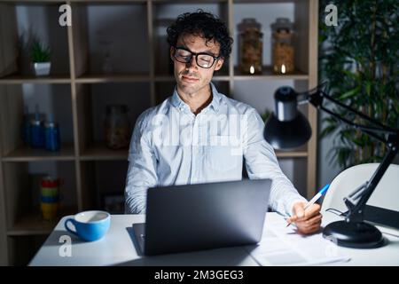 Homme hispanique travaillant au bureau la nuit, regardant somnolent et fatigué, épuisé pour la fatigue et la gueule de bois, les yeux paresseux le matin. Banque D'Images