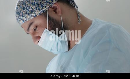 Professionnel de la santé de sexe masculin caucasien dans un bloc opératoire d'hôpital portant un capuchon et un masque chirurgicaux. Action. Chirurgien pendant l'intervention Banque D'Images