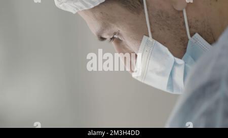 Professionnel de la santé de sexe masculin caucasien dans un bloc opératoire d'hôpital portant un capuchon et un masque chirurgicaux. Action. Chirurgien pendant l'intervention Banque D'Images