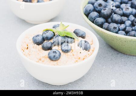 Porridge de flocons d'avoine garni de myrtille et de feuilles de menthe dans un bol blanc sur la table. Recette de porridge du matin. Idées de petit déjeuner sain Banque D'Images