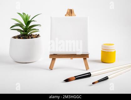 Nettoyer la maquette de toile vierge pour la peinture, le dessin sur chevalet, les pinceaux, la plante en pot et la gouache jaune. Photo de haute qualité Banque D'Images
