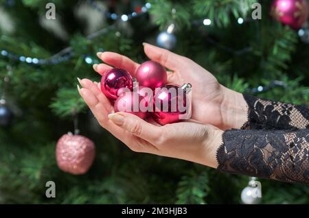 Gros plan des mains de femmes tenant une poignée de boules de Noël sur le fond des branches de sapin Banque D'Images