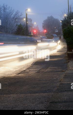 Circulation en banlieue : en hiver, les voitures descendent une pente douce, les phares se flent sous les lampadaires éclairés et les feux de circulation s'allument Banque D'Images