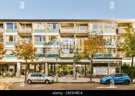 deux voitures garées devant un immeuble de plusieurs étages avec des madriers sur le côté et des arbres bordant la rue Banque D'Images