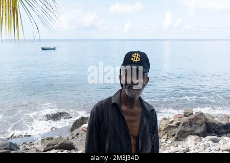 Dominique, Roseau - 12 novembre 2022: Portrait d'un homme senior de Dominique, des Caraïbes avec fond flou d'eau et plage rocheuse Banque D'Images