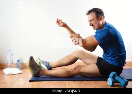 Homme faisant du sport à l'intérieur se plaignant de douleurs d'avant-bras assis sur un tapis. Vue latérale Banque D'Images