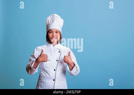 Sympathique cuisinier positif faisant le pouce vers le haut geste approuvant la recette gastronomique, la cuisine du dîner culinaire à l'aide d'ingrédients sains. cuisson réussie montrant le panneau d'approbation, préparation du plat alimentaire Banque D'Images
