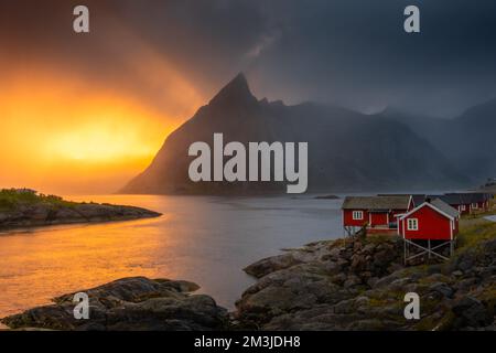 Coucher de soleil incroyable à travers la brume et le Mont Reinebringen sur les maisons rouges de Hamnoy, îles Lofoten, Norvège Banque D'Images