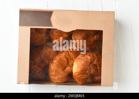 Six petits pains Croissant dans une boîte de boulangerie, sur une table rustique en bois blanc. Banque D'Images