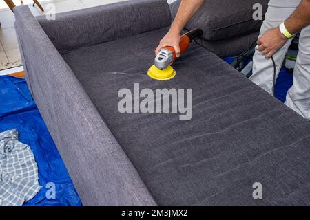 Homme utilisant une brosse de polissage électrique pour nettoyer les coussins du canapé. Banque D'Images