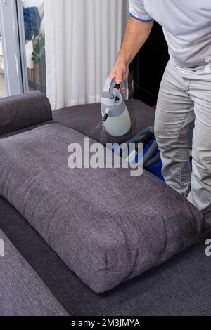 Homme versant un liquide pour nettoyer et imperméable coussins de canapé vertical. Banque D'Images