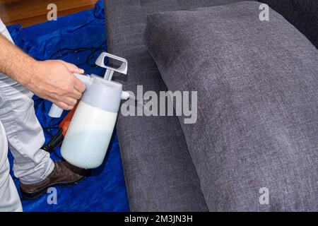 Gros plan d'une main d'homme versant un liquide pour nettoyer et imperméable les coussins du canapé. Banque D'Images