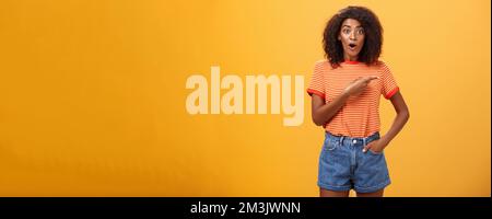 Photo en studio d'un modèle féminin élégant en short denim et un t-shirt qui se déva a impressionné de pointer du bon côté tout en posant la question intéressé pendant Banque D'Images