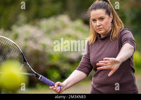 une joueuse de tennis pratiquant les mains avant et frappant des balles de tennis sur un terrain d'herbe en angleterre Banque D'Images