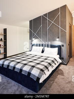 Intérieur minimaliste de la chambre avec grand lit intérieur. Vue avant du grand lit, avec couverture en tissu écossais contre le mur gris et décoration géométrique dans la chambre. Concept d'intérieur. Banque D'Images