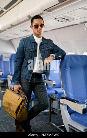 Portrait, beau et attrayant homme de voyage asiatique en jean veste et lunettes de soleil se tient dans l'allée portant ses bagages. touriste, voyageur, passager Banque D'Images