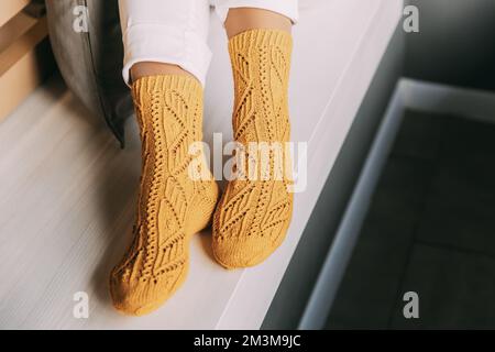 Gros plan des jambes des femmes en chaussettes d'hiver tricotées jaunes, pantalon blanc reposant sur un banc au café en hiver. Journée de repos en chaussettes tricotées à Banque D'Images
