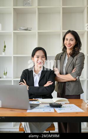 Portrait, deux femmes d'affaires asiatiques confiantes et réussies en costumes d'affaires sont au bureau, les bras croisés, souriant, et regardant la caméra. Banque D'Images