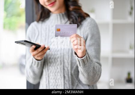 Image rognée, belle jeune femme asiatique en chandail gris tenant un smartphone et une carte de crédit. Banque D'Images